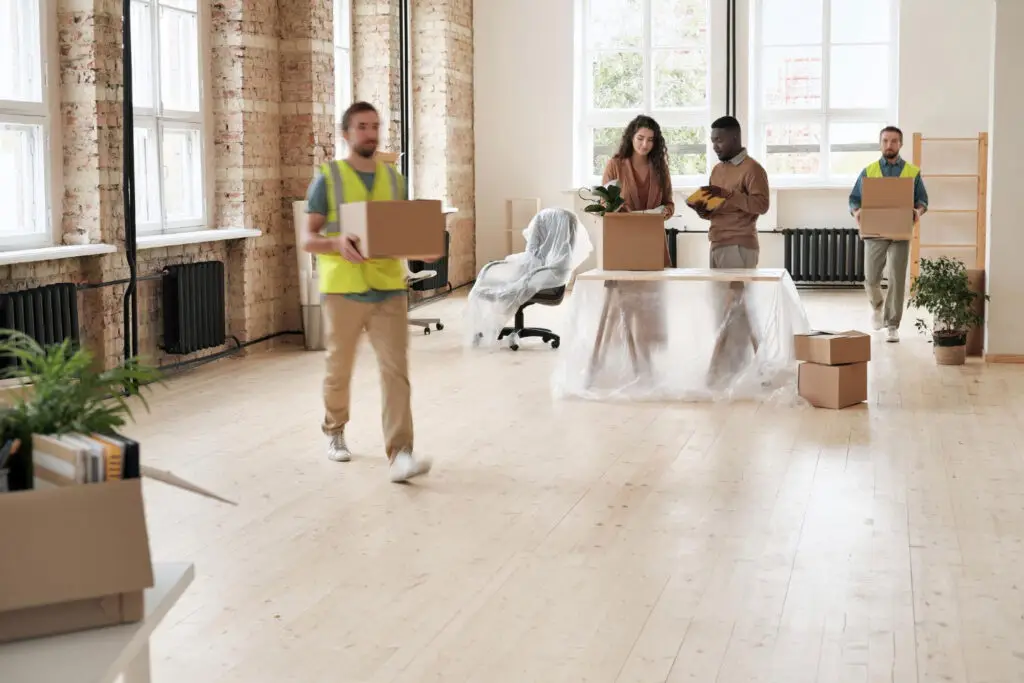People carrying boxes and covered furniture in a spacious room preparing for a move-out cleaning checklist.