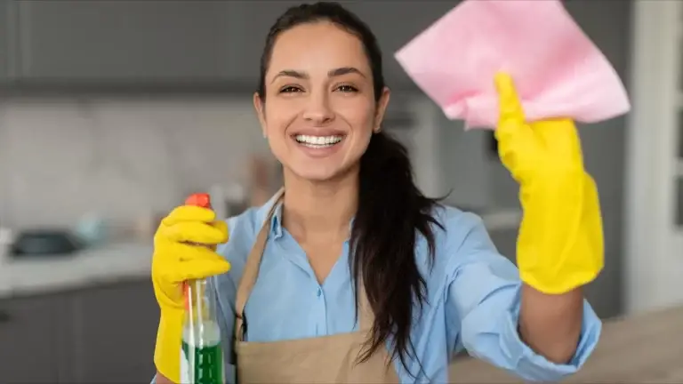 Smiling woman holding a spray bottle and a pink cloth.