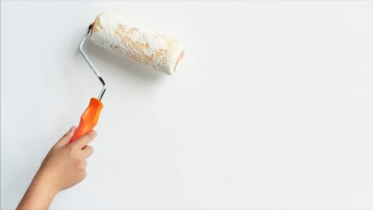 Hand holding paint roller on white wall