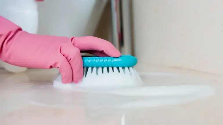 Gloved hands scrubbing bathroom floor with brush