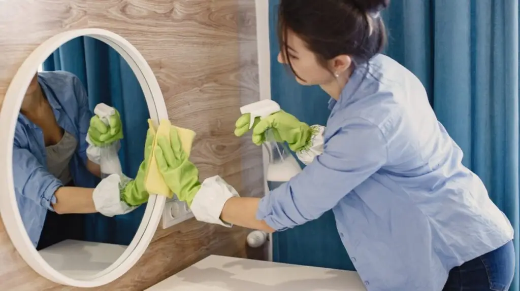 Woman cleaning bathroom mirror with spray
