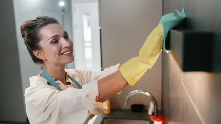 Woman with yellow gloves cleaning kitchen cabinet