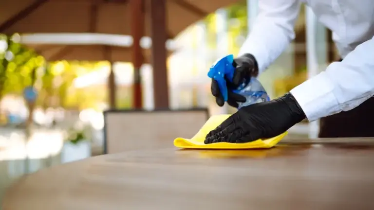 Staff member disinfecting outdoor restaurant table with spray and yellow cloth