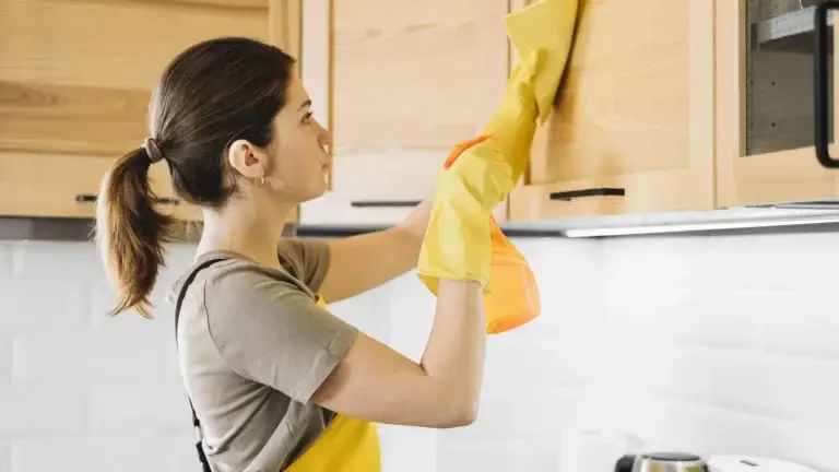 Woman in yellow gloves cleaning a kitchen cabinet
