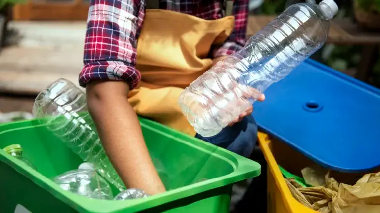 Person sorting plastic bottles into recycling bins